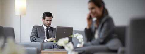 Bild: Zwei Business-Leute sitzen in der Hotel Lobby und arbeiten am Laptop.